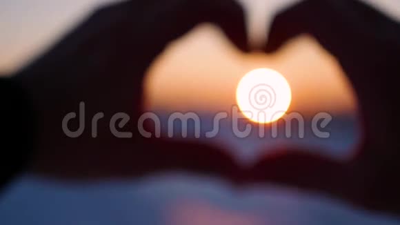 女孩用手在阳光下做心脏剪影手中的心形与里面的夕阳冬季视频的预览图
