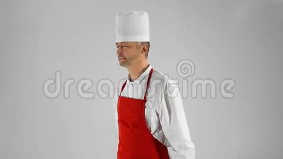 英俊的成年厨师转过身来他用刀子交叉双臂在灰色背景上点头视频的预览图