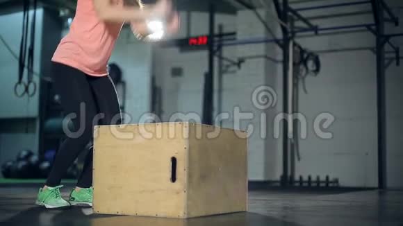 年轻的强壮的女人穿着运动服在健身房做一套盒子跳跃女孩跳到木头上视频的预览图