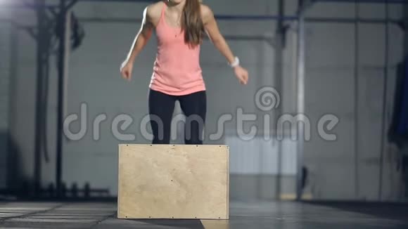 年轻的强壮的女人穿着运动服在健身房做一套盒子跳跃女孩跳到木头上视频的预览图