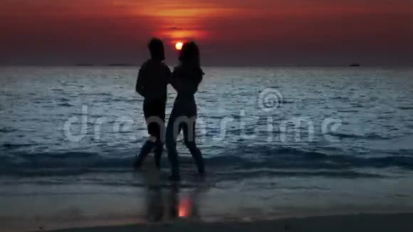 男人和女人的剪影在日落时出海在海浪中接吻视频的预览图
