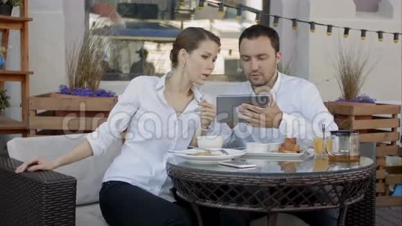 两个年轻人在咖啡店开会时使用数码平板电脑视频的预览图