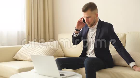 与同事保持联系穿着衬衫的帅哥在笔记本电脑上工作在手机上说话视频的预览图