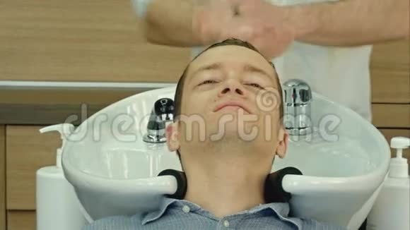 年轻人闭着眼睛躺在美容院里英俊的男人在美发沙龙洗头发视频的预览图