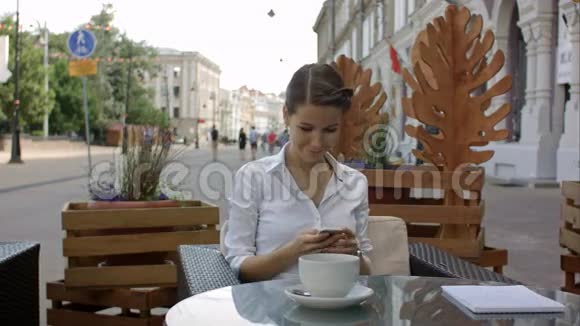 年轻女子在户外咖啡馆喝咖啡用手机视频的预览图
