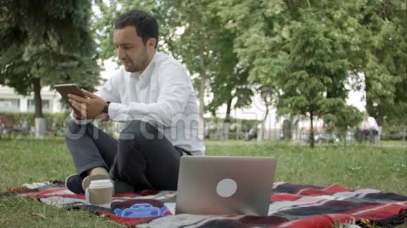 年轻的成功商人在公园里使用平板电脑笔记本电脑和手机视频的预览图