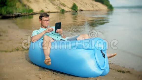 一个男人正在海边的充气床垫上休息他用的是平板电脑视频的预览图