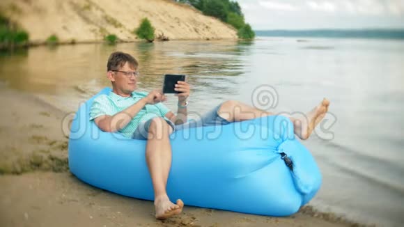 一个男人正在海边的充气床垫上休息他用的是平板电脑视频的预览图