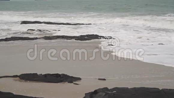 在岩石和沙滩上冲浪阴天拍摄慢动作视频视频的预览图