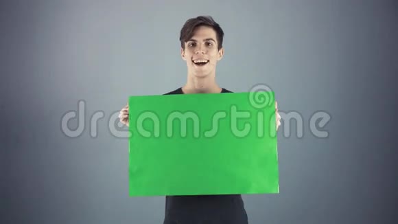 喜出望外的年轻人穿着黑色衬衫拿着绿色钥匙片海报灰色背景视频的预览图