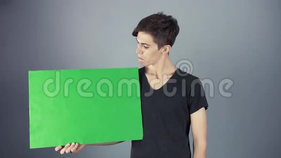 穿着黑色衬衫的年轻人拿着绿色钥匙片海报灰色背景视频的预览图