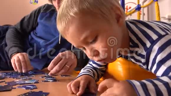 父亲和他的金发小儿子一起组装拼图男人和他的小男孩在家有空闲时间4K视频视频的预览图