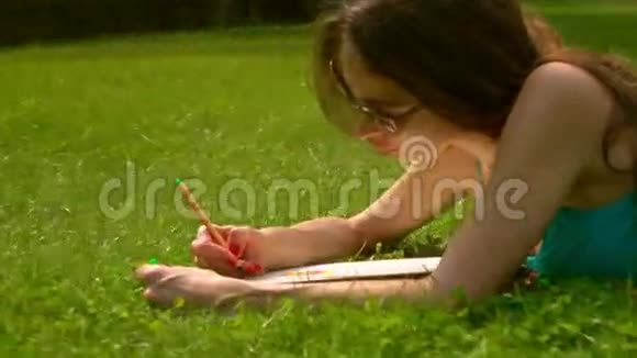 美丽的黑发女孩戴着太阳镜躺在草地上画画4克斯泰德姆视频的预览图