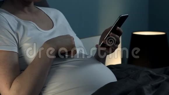 怀孕的女人带着电话坐在床上视频的预览图