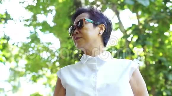 视频酷亚洲资深女士戴着绿色自然背景的太阳镜白色衬衫视频的预览图