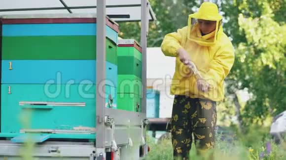 夏天一个年轻的养蜂人在养蜂场里清理木制的蜂蜜架视频的预览图