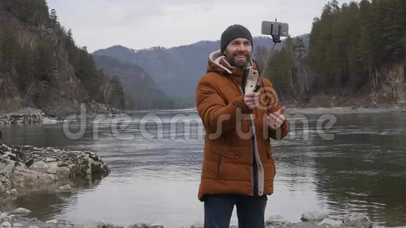 留胡子的游客在一条山河岸的手机上拍照慢动作视频的预览图