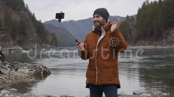 留胡子的游客在一条山河岸的手机上拍照慢动作视频的预览图