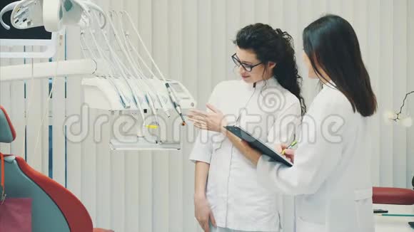 一位微笑的牙医和助手的肖像看着现代牙科诊所的剪贴板穿着医疗服装视频的预览图