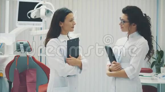 一位微笑的牙医和助手的肖像看着现代牙科诊所的剪贴板穿着医疗服装视频的预览图