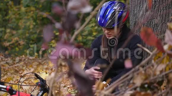 一个年轻的女人从自行车上摔下来后坐在公园里平静膝盖的疼痛在公园里骑一辆危险的自行车视频的预览图