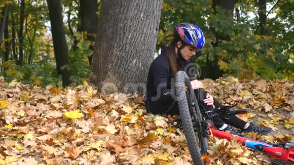 一个年轻的女人从自行车上摔下来后坐在公园里平静膝盖的疼痛在公园里骑一辆危险的自行车视频的预览图
