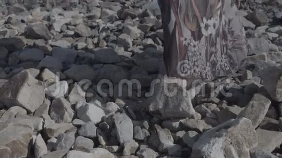 一个女人穿着一件长裙子站在大石头上平坦的颜色仔细观察她的脚视频的预览图