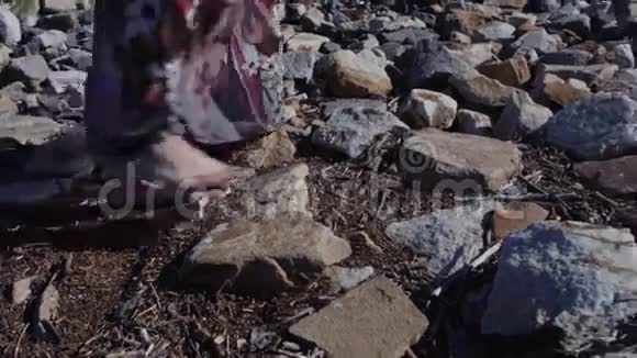 一个女人穿着一件长长的连衣裙站在地面上的大石头上仔细观察她的脚视频的预览图