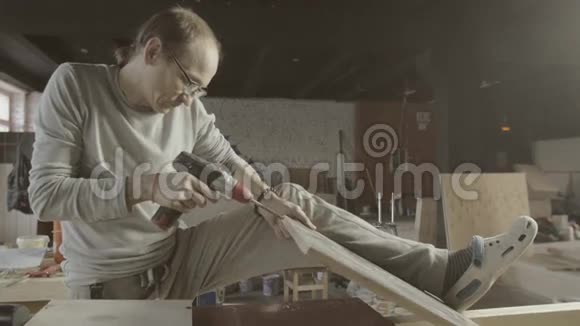 木工用电钻在抛光的木板上打孔用腿固定木板视频的预览图