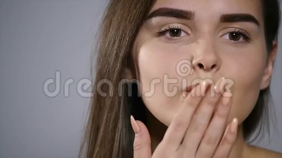 一位深褐色头发的漂亮女孩的特写镜头透过镜头在灰色的摄影棚墙壁背景上亲吻视频的预览图