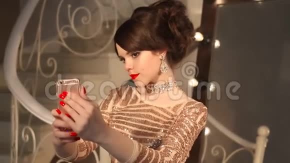 赛尔夫年轻的少女穿着金色的裙子和珠宝拍照优雅的女士穿着亮片连衣裙摆着镜子视频的预览图