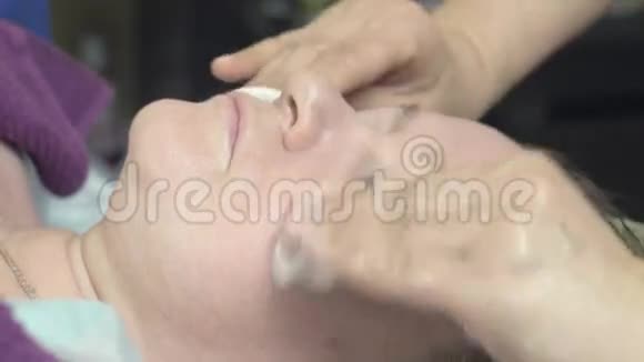 美容师用清洁棉垫擦拭美容店里厚厚的女人的脸视频的预览图