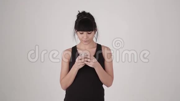 西班牙拉丁裔漂亮女孩在智能手机上发短信在灰色背景下微笑复制空间文本视频的预览图