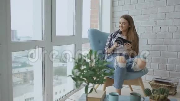 有魅力的女性使用数码平板电脑坐在阁楼的阳台上的椅子上视频的预览图