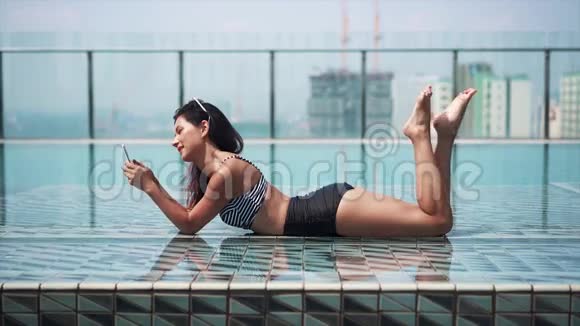 快乐的女人在泳池边用智能手机视频的预览图