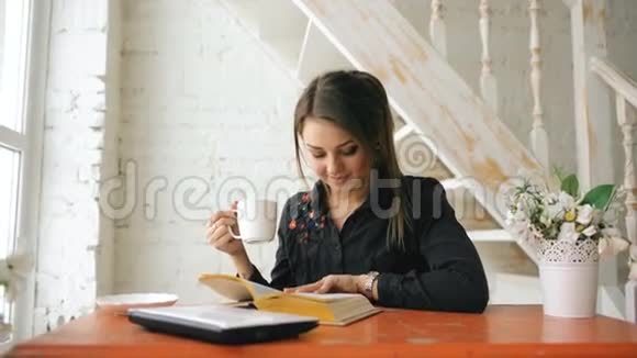 年轻漂亮的女学生坐在室内咖啡厅的笔记本电脑上看书视频的预览图