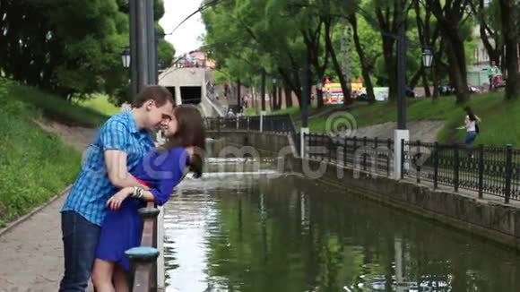 男人倚着女人亲吻她在公园的小河边视频的预览图