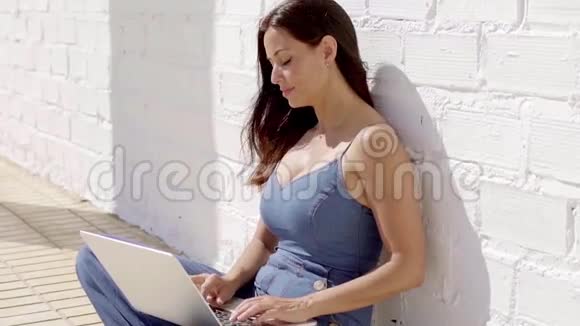 穿着笔记本电脑坐在阳光下的漂亮女人视频的预览图