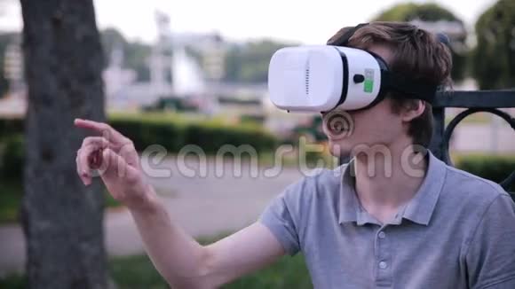 年轻的帅哥戴着虚拟现实护目镜坐在城市公园里视频的预览图