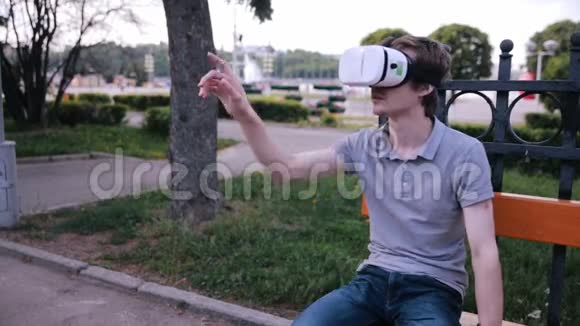 年轻的帅哥戴着虚拟现实护目镜坐在城市公园里视频的预览图