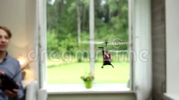 一个漂亮的男孩在家里玩一架红色玩具直升机下一架直升机在窗户里飞视频的预览图
