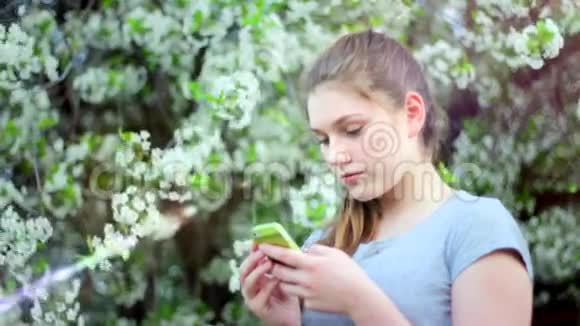 公园里有智能手机的少女春天在一棵开花的树的背景下视频的预览图