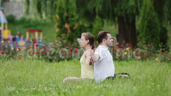 一个男人和一个女人在做运动之前伸展身体年轻的瑜伽教练在绿草如茵的城市公园练习视频的预览图
