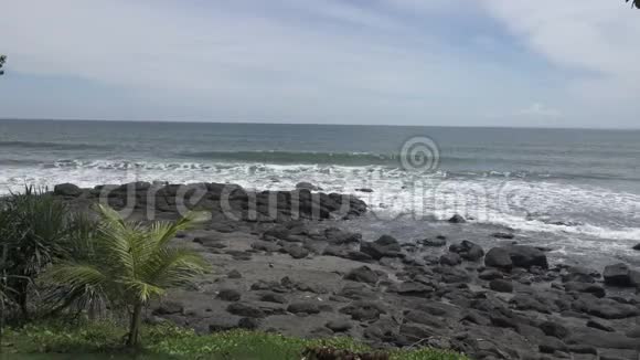 热带海洋的海岸在阳光明媚的日子里海浪带着黑色的石头在海岸上奔腾视频的预览图