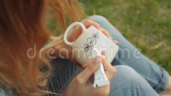 特写女性手在白色杯子上画图案女孩在晚上坐在草地上画装饰品视频的预览图