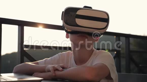 这个男孩正在电脑上玩虚拟现实眼镜在日落时现代概念视频的预览图