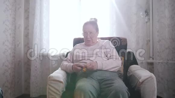 一位老妇人喜欢坐在椅子上在窗户的背景上编织视频的预览图