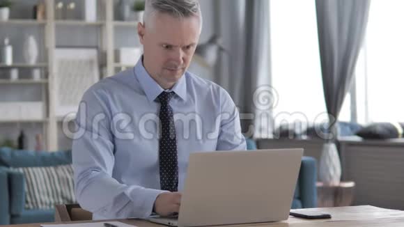 灰色头发商人在笔记本电脑上工作视频的预览图
