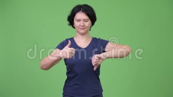 美丽的女人留着短发在竖起大拇指和向下大拇指之间做出选择视频的预览图
