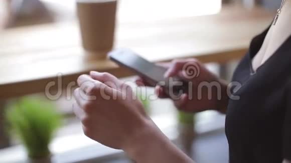 年轻女子喝着咖啡坐在室内的城市咖啡馆里使用智能手机视频的预览图